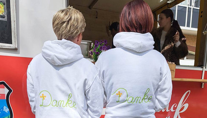 Zwei Mitarbeiterinnen stehen mit hellen Sweatshirts mit der Aufschrift "Danke" vor einem Food-Truck am Internationalen Tag der Pflegenden auf dem Außengelände des Immanuel Klinikums Bernau Herzzentrum Brandenburg. 