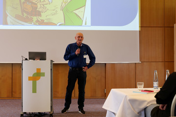 Ein Arzt in Alltagskleidung steht mit einem Mikrofon auf dem Podium vor einer Leinwand neben einem Sprechpult und hält einen Vortrag bei der Fachveranstaltung 11. Amalie Tag der Hausärztinnen und Hausärzte im Evangelischen Amalie Sieveking Krankenhaus in Hamburg-Volksdorf. Ein Arzt in Alltagskleidung steht mit einem Mikrofon auf dem Podium vor einer Leinwand neben einem Sprechpult und hält einen Vortrag bei der Fachveranstaltung 11. Amalie Tag der Hausärztinnen und Hausärzte im Evangelischen Amalie Sieveking Krankenhaus in Hamburg-Volksdorf.