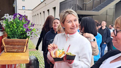 Eine Mitarbeiterin hält Burger und eine Beilage vor einem Food-Truck in den Händen und blickt am Internationalen Tag der Pflegenden im Immanuel Klinikum Bernau Herzzentrum Brandenburg in die Kamera.